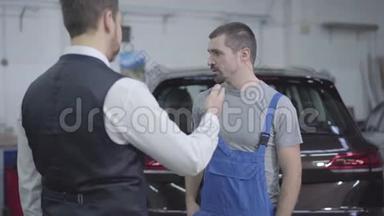 年轻的白种人穿着工作袍，在修理厂拿着顾客的车钥匙，摇着手。 汽车修理工开车