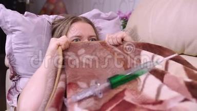 在家被隔离的患病女孩躲在毯子下面，看到注射疫苗的注射器
