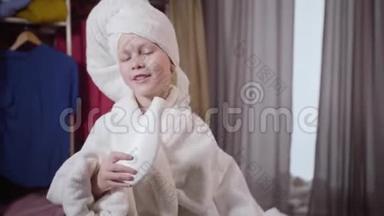 穿着白色浴袍和发巾在家唱歌的可爱白种人女孩的肖像。 使用洗发水瓶的快乐儿童