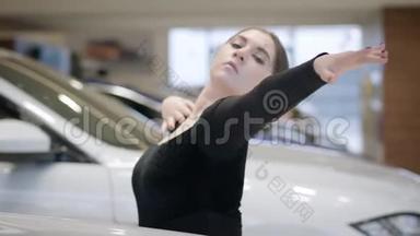 自信的高加索芭蕾舞演员在汽车经销店跳舞。 女芭蕾舞演员在白色汽车间穿梭