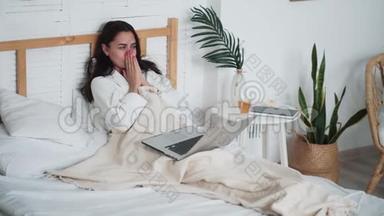 疲惫的女人坐在床上，在家里用笔记本电脑工作，伸懒腰打哈欠