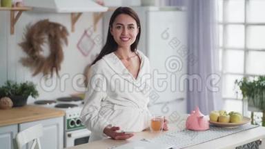 身着白色浴袍的年轻女子早晨在厨房喝茶的肖像