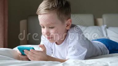 可爱的小男孩蹒跚学步，<strong>玩手机</strong>游戏，躺在床上，拿着智能<strong>手机</strong>
