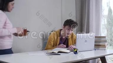 镜头靠近疲惫聪明的白人男孩，他正在桌边写字，妈妈端着茶和糖果走过来。忧心忡忡
