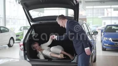 成年白种人男子打开汽车后备箱，帮助开朗优雅的女人下车。 有钱的女商人
