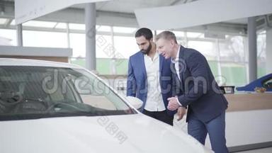 两个成年人在经销商店里讨论新的白色汽车。 高加索经销商和中东客户在陈列室交谈