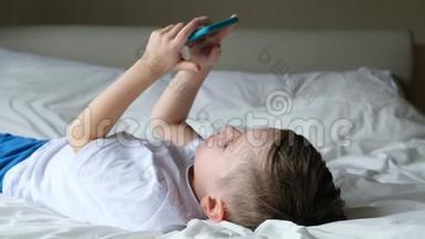 可爱的小男孩蹒跚学步，<strong>玩手机</strong>游戏，躺在床上，拿着智能<strong>手机</strong>