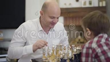 快乐白种人和儿子下棋的肖像。 微笑聪明的父亲在家教育孩子。 家庭