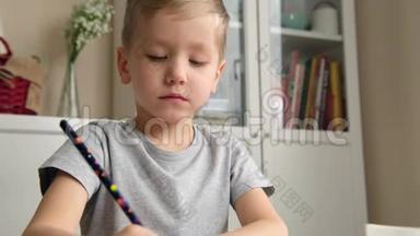 学龄前男孩幼儿，拿着铅笔，在桌子旁画画或做作业