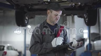 自信的成人维修工程师站在维修车间的车<strong>底下</strong>，使用电脑。 白种人汽车