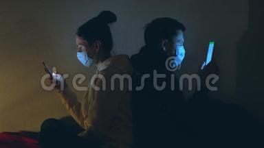 年轻夫妇戴着医用口罩，晚上使用智能手机和笔记本电脑。