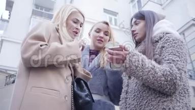 三个高加索女孩使用智能手机寻找位置的底部视图。 美丽的年轻女子在谈话和寻找