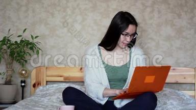 年轻漂亮的女孩正在用她的笔记本电脑工作，<strong>坐在</strong>家里的<strong>床上</strong>。 年轻可爱的女孩正<strong>坐在床上</strong>打字