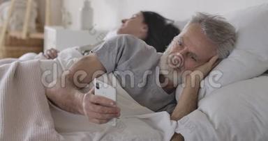 高加索人躺在床上用智能<strong>手机</strong>做妻子睡在<strong>后台</strong>的特写照片