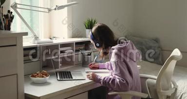 戴着耳机在<strong>网上学习</strong>的少女用笔记本做笔记