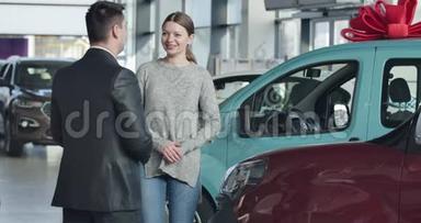 <strong>年轻笑</strong>容可掬的高加索女人和汽车经销店的商人交谈。 陈列室里站在新车旁边的人
