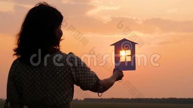 一个女人做梦，拿着纸屋，看着夕阳。 纸屋的剪影。