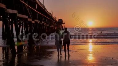 加州圣克莱门塔，一对夫妇在美丽的橙色、粉红色日落处散步，在阳光和太阳耀斑的木墩上散步