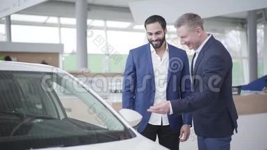 积极的白人经销商与富有的中东客户在炫耀和传递汽车钥匙。 自信的富人