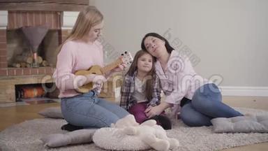 <strong>漂亮</strong>的金发白种人女孩在家为母亲和妹妹演奏四弦琴。 天<strong>才</strong>少年娱乐家庭