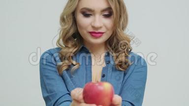可爱的女人在一张桌子上拿着一个苹果，背景是水果和蔬菜。