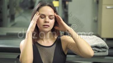 年轻有魅力的女人在健身房积极锻炼后，用<strong>毛巾</strong>休息并<strong>擦拭</strong>脸上的汗水。