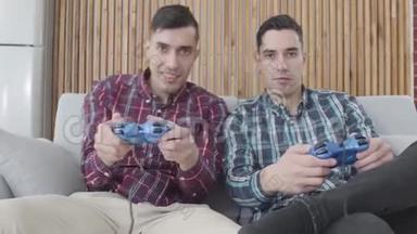 两个积极的白人男子在电子游戏中竞争。 一个穿红衬衫的男人在他的双胞胎兄弟离开时，用手指指着他