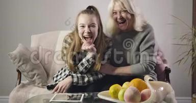 快乐的白人祖母和孙女一起看电视和大笑的肖像。 积极的家庭<strong>开支</strong>