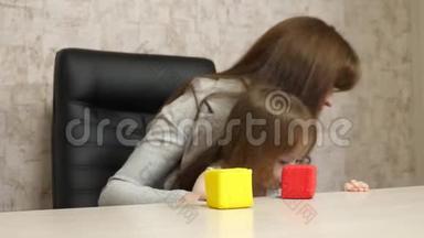 妈妈在办公室里和她的孩子在工作时用多种颜色的立方体玩耍。 忙碌的女人拿着婴儿在工作