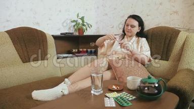 一位穿着浴袍的妇女在家里的沙发上患流感症状，<strong>测量体温</strong>