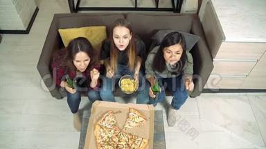 三个年轻的女人喝着啤酒，看着电视在她们最喜欢的球队欢呼，在家的客厅里为进球而欢呼