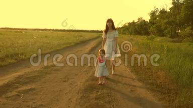 妈妈和宝宝在公园休息。 快乐童年的概念。 小女儿和妈妈沿着马路经过田野。 儿童