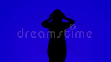 一位身材苗条的<strong>女士</strong>戴着耳机，在蓝色背景下随着音乐起舞的<strong>剪影</strong>