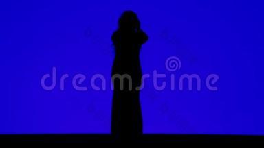 一个戴着耳机的苗条女人在蓝色背景下<strong>随</strong>着<strong>音</strong>乐起舞的剪影