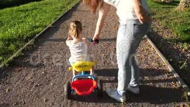 妈妈教女儿在公园里骑自行车。 幼儿学习骑自行车.. 妈妈玩她的小东西