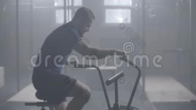 年轻的活跃男子在健身房旋转空气自行车。 男子慢动作的空中自行车训练。 中型健身男子工作