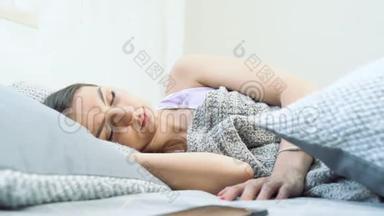 熟睡的年轻女子关掉手机上的闹钟，把它藏在枕头下，继续睡觉