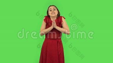 穿着红色衣服的温柔女孩把手掌放在一起，要求一些东西。 绿色屏幕