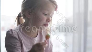 一个小女孩看着窗外，在棍子上吃糖果