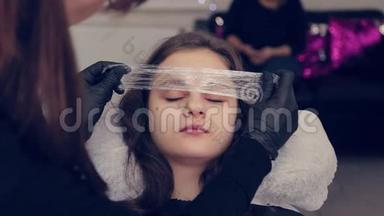 专业的女眉大师在一家美容院把眉毛上的胶卷放在眉毛上。