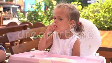 可爱的小白种人女孩在餐桌上吃意大利面，坐在儿童座椅户外餐厅。