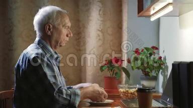 一个吃汉堡的老人晚上在家里用笔记本电脑看电影或电视节目。
