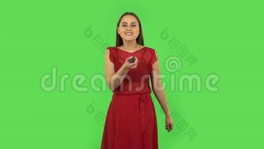 一个穿着红色连衣裙，手里拿着电视遥控器，打开电视的小女孩。绿色屏幕