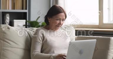 中年老年妇女用坐在沙发上的笔记本电脑打字