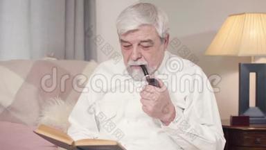 白发苍苍的白人男子在家抽烟斗和<strong>看书</strong>的肖像。成熟严肃的男人度过<strong>安静</strong>的夜晚