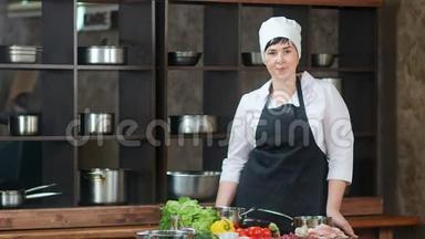 微笑女厨师穿围裙在餐厅厨房内部摆姿势。 中型摄影机