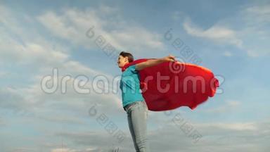 孩子穿着红色外套玩，梦想成为英雄女<strong>超人</strong>。 美丽的女孩超级英雄站在红色的田野上