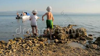 两个快乐的白种人孩子，兄弟，一起玩，把石头扔进海里。 小兄弟在户外玩耍