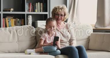 快乐的老奶奶和可爱的孙女在家里使用智能手机