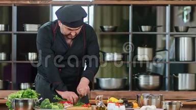 英俊的男厨师穿黑色制服切割绿色和胡椒。 中型摄影机